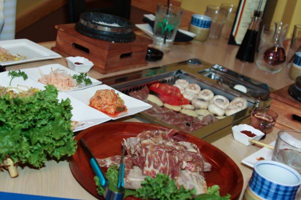 Kalbi on the grill in the center of a table along with vegetables.