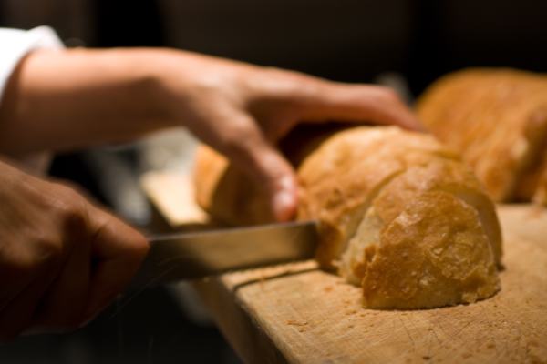 Freshly baked bread being sliced before being taken to your table with a thick slice of butter, sprinkled with sea salt.
