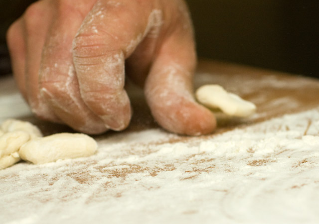 The slightly flattened and curled pasta dough flips over Chef\'s thumb.