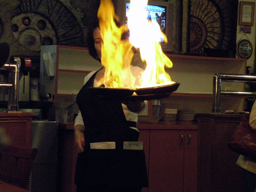 Waitress Toula lights two orders of saganaki.  It\'s widely believed that The Parthenon in Greektown originated the practice of flambe&#233ing saganaki tableside in the 1960\'s.
