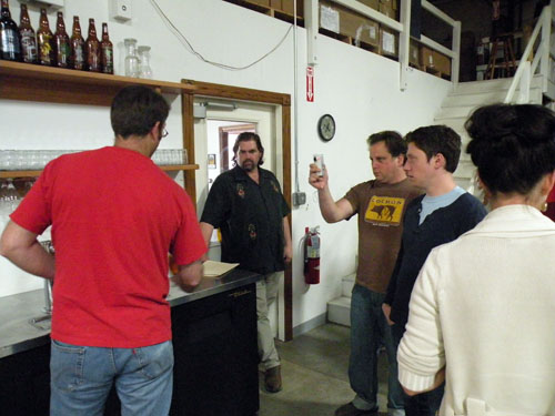 Bueltmann enters the brewery as Haggerty pours some oak-aged Mad Hatter and Kahan uses a Flip video camera.
