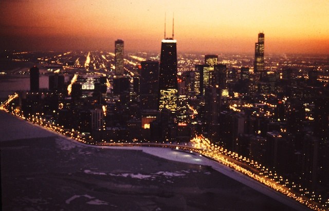 Around New Year\'s 1980 I told my old friend and client Chuck Percy, president of Bell & Howell and later Senator of Illinois, that \<em\>Reader\'s Digest\<\/em\> had hired me to shoot Chicago from the air at night, something almost impossible to do well at the time given the limits of lenses and film. Chuck, whom I had shot for \<em\>Fortune\<\/em\> and whose family Christmas pictures I did for fun, handed a beautiful camera across his desk. A Canon VII. It had a huge, Canon .095 lens on it. Number 60. It was, outside the space program, the fastest lens in the world. He gave the rig to me on permanent loan. So the picture above was made with that gorgeous lens wide open and with the Canon shutter at 1/250th of a second.Ektachrome 100 pushed a stop. For $80 I hired an amateur pilot I liked whose daytime job was as a \<em\>Sun-Times\<\/em\> reporter. My first flight with Carl Lavin had been to photograph Gary for \<em\>Chicago\<\/em\> magazine. My beautiful daughter had come along to change film for me and work my nack-up camera- and it was love at first flight- They were married a year later and presented Florence and me with three grandsons and a grand-daughter (and soon to be great-grandchild!).  I just called an old writer friend to tell her of this picture showing her pad, Oak Street Beach as it was 30 years ago and the New Yearâs snow forming on the lake shore. She invited me to drop in - without the plane - any old time. She and I worked on the Speck murder story, and she was grateful to me for correcting the spelling of one word. Rackets, as in racketeer - she misspelled, society chick that she was, as racquets. My pilot\'s wife, daughter Lauren, would live for a time on the 44th floor of the Hancock Building, just above that tiara of lights. Again, as Studs said, \"It\'s all connected isn\'t it.\"