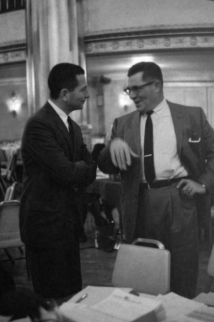 In the mid sixties SI sent me to cover the NFL trade negotiations in downtown Chicago. The magazine\'s interest was largely in the horse trading between Vince Lombardi and Bears owner George Halas. But this picture became my favorite. It sounded a personal note for me that still rankled my ego! The younger trader on the left looked suddenly familiar. Then I remembered! He was non other than Allie Sherman, the coach of the New York Giants! The very NFL star back who a mere quarter century ago had beaten me out of the job of first string quarterback for the Brooklyn College freshman team a mere quarter century previous, in 1942!\r\nIt was two eras before the male hug so we just shook hands- and I had the pleasure of describing to Lombardi our first day of practice: \"It was muddy- and Allie who weighed what I did - 170 - and was an inch taller, was wearing mud cleats.\r\n\" Yes. Mud cleats ! From high school. About an inch long.\" \r\nHe slapped his brow. \"I remember! We both punted and my cleats caught - and I went down on my ass...!\" Lombardi roared . \"Punting with mud cleats!\" Then I told the rest of the story as Allie smiled. \"The Brooklyn Dodgers trained on our field,\" I began- \r\nAllie picked up the memory. \"Drummond-\"\r\n\"Bulldog Drummond,\" Lombardi put in. \"He wrestled.\" \r\n\"Bulldog stood there five yards away and put out his arms sideways. \"Run at me, kids,\" he said  then shook his head and grimaced.\"\r\n\"It was like hitting a horizontal steel post,\" I said.\"We both doubled up over his giant arms.\"\r\n\r\nIn that moment I knew I\'d never amount to much as a football player-but Allie went on to become an NFL running back and to successfully manage the NY Giants for eight years. I went on to war instead.