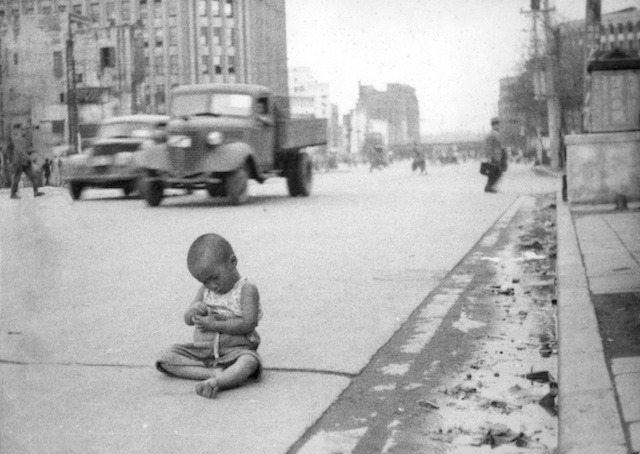 On one of downtown Tokyo\'s dangerous main arteries an untended waif sits - a serene image related to the famous one made years earlier during Japan\'s conquest of Manchuria. A picture in which another homeless waif bawls his head off. We moved the kid to safety and filled his tiny pockets with yen.