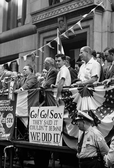Hizzoner, at left, on a joyous day in front of City Hall in 1959, addresses the passing parade of players and celebrants hardly able to believe the Sox had won the pennant. The Dodgers went on to beat them 4 games to 2 in the World Series. I think that\'s Bill Daley holding the sign, and bald Bill Veeck shifting uncomfortably on his one real leg. Daley often bolluxed his favorite Veeck anecdote, which was basically: \"Bill had to have his leg amputated a few years ago for reasons of his health. And he says even with great Chicago medical care it cost him an arm and a leg.\"