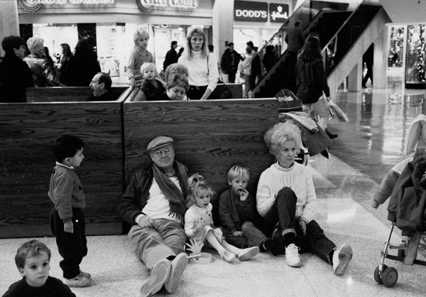 At the end of a day spent chasing their grandkids through the purlieus of Northbrook Court, two loving grandparents plop down for a break on the only vacant seats: The linoleum. The guy yawning in the background pew is a gift of chance to the fotog. [Image Credit: Art Shay]