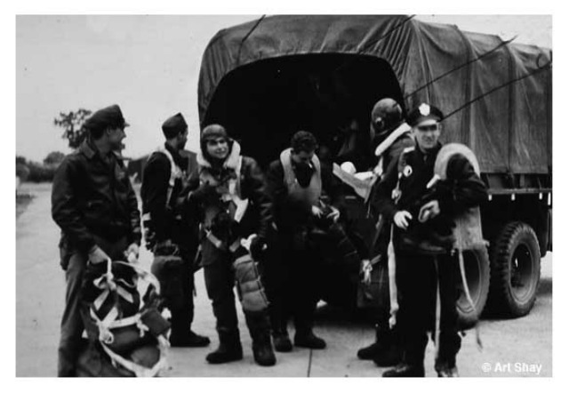 This is our crew: pilot Cecil B. Isom on the right, I\'m third from left, parachute on leg. We\'re ready to board truck and ride out to hardstand and board Sweet Sue. We stand on the very tarmac I would do evasive action on to escape  the panicking Colonel who tried to stop me from shooting the mid-air collision and aftermath. \"It\'s restricted,\" he kept yelling. I kept shooting, great training for when, three years later, I went to work for \<em\>Life\<\/em\> as a reporter and, three years after that as a photographer-reporter.
