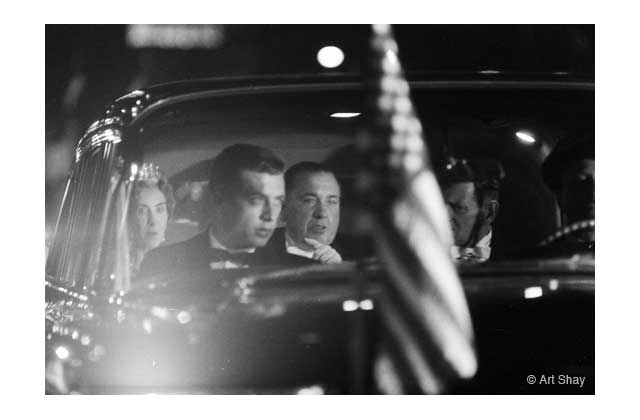 King Frederick IX and Queen Ingrid of Denmark [October 1960] tour Chicago at night under guidance of Mayor Richard J. Daley visible through an official welcoming flag.\r\n