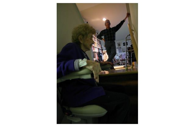 Dan, holding onto a handrail he installed, supervises Florence\'s first trip up the lower of two stair lifts he insisted she have. Her ovarian cancer\'s first two blows took away her walking and her hearing.\r\n